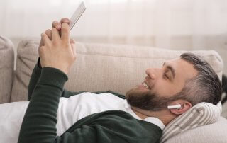 Cheerful man watching movies on digital tablet with wireless earphones